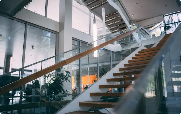 Modern staircase with glass railings and wooden steps in a bright, open-plan building. Modern staircase with glass railings and wooden steps in a bright, open-plan building.